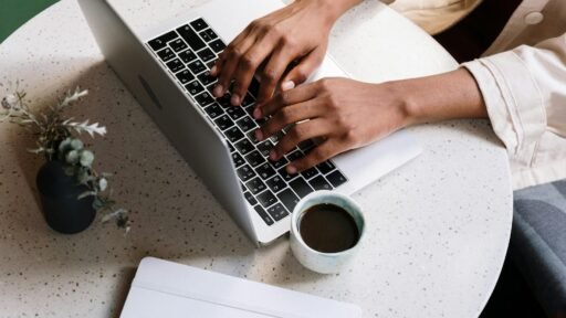 person using macbook pro beside white ceramic mug